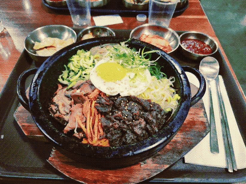 A picture of a colorful stone bowl of bibimbap with banchan in the background.